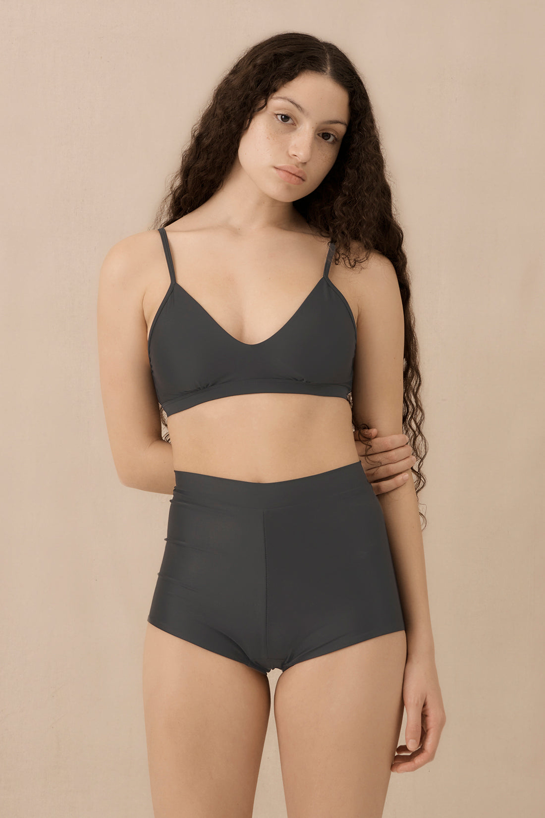 Woman wearing blueish grey high waist surf shorts, sustainable swimwear designed to stay on in the surf, offering supportive coverage and a flattering fit for active beach days.