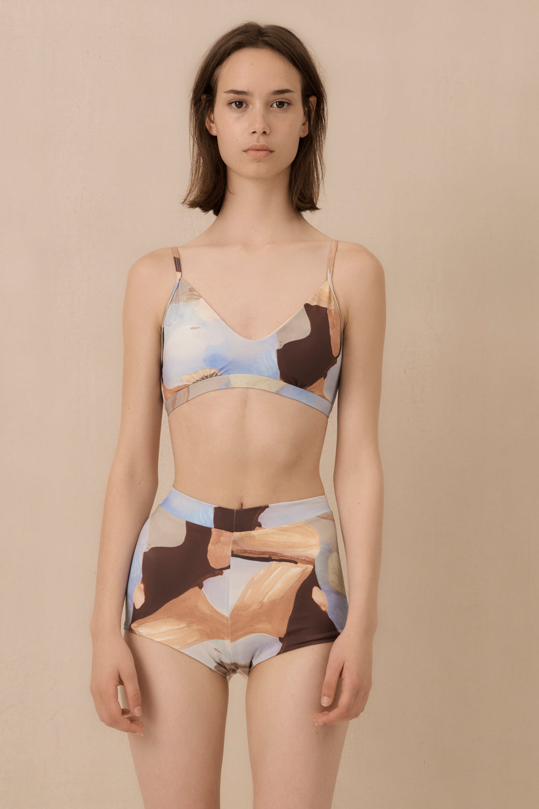 Woman wearing mirador artist print high waist surf shorts, sustainable swimwear designed to stay on in the surf, offering supportive coverage and a flattering fit for active beach days.