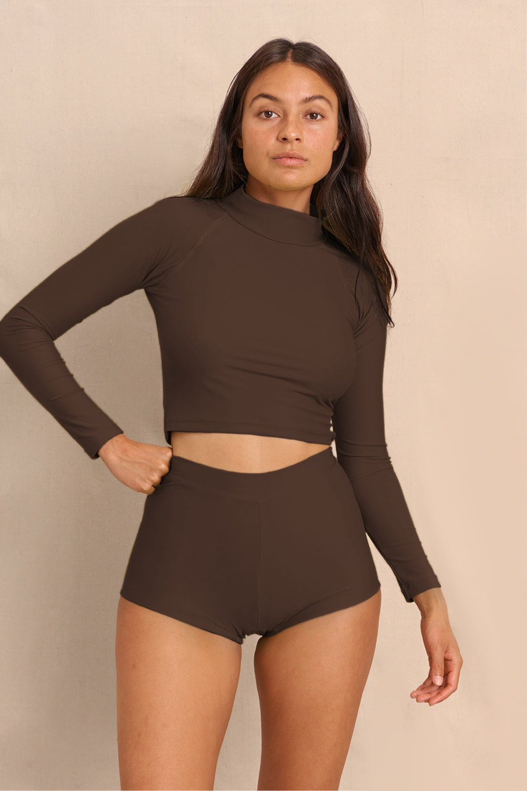 Woman wearing brown Aire Turtle Neck a high neck, minimalist long sleeve women’s rashguard made from sustainable fabric, designed for sun protection and surf performance.