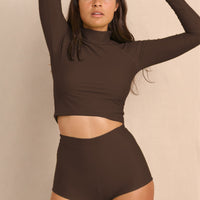 Woman wearing brown Aire Turtle Neck a high neck, minimalist long sleeve women’s rashguard made from sustainable fabric, designed for sun protection and surf performance.