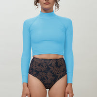 Woman wearing blue Aire Turtle Neck, a high neck, long sleeve women’s rashguard made from sustainable fabric, designed for sun protection and surf performance.