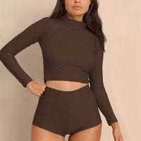 Woman wearing brown high waist surf shorts and matching rashguard, sustainable swimwear designed to stay on in the surf, offering supportive coverage and a flattering fit for active beach days.