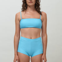 Woman wearing blue high waist surf shorts, sustainable swimwear designed to stay on in the surf, offering supportive coverage and a flattering fit for active beach days.