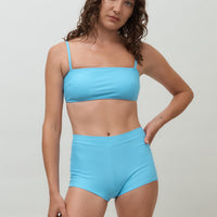 Woman wearing blue high waist surf shorts, sustainable swimwear designed to stay on in the surf, offering supportive coverage and a flattering fit for active beach days.
