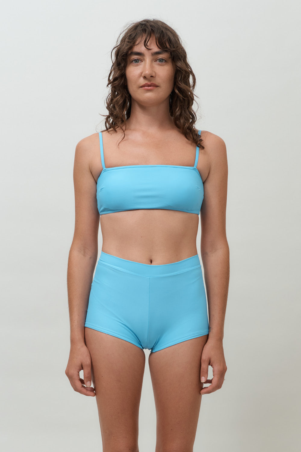 Woman wearing blue high waist surf shorts, sustainable swimwear designed to stay on in the surf, offering supportive coverage and a flattering fit for active beach days.