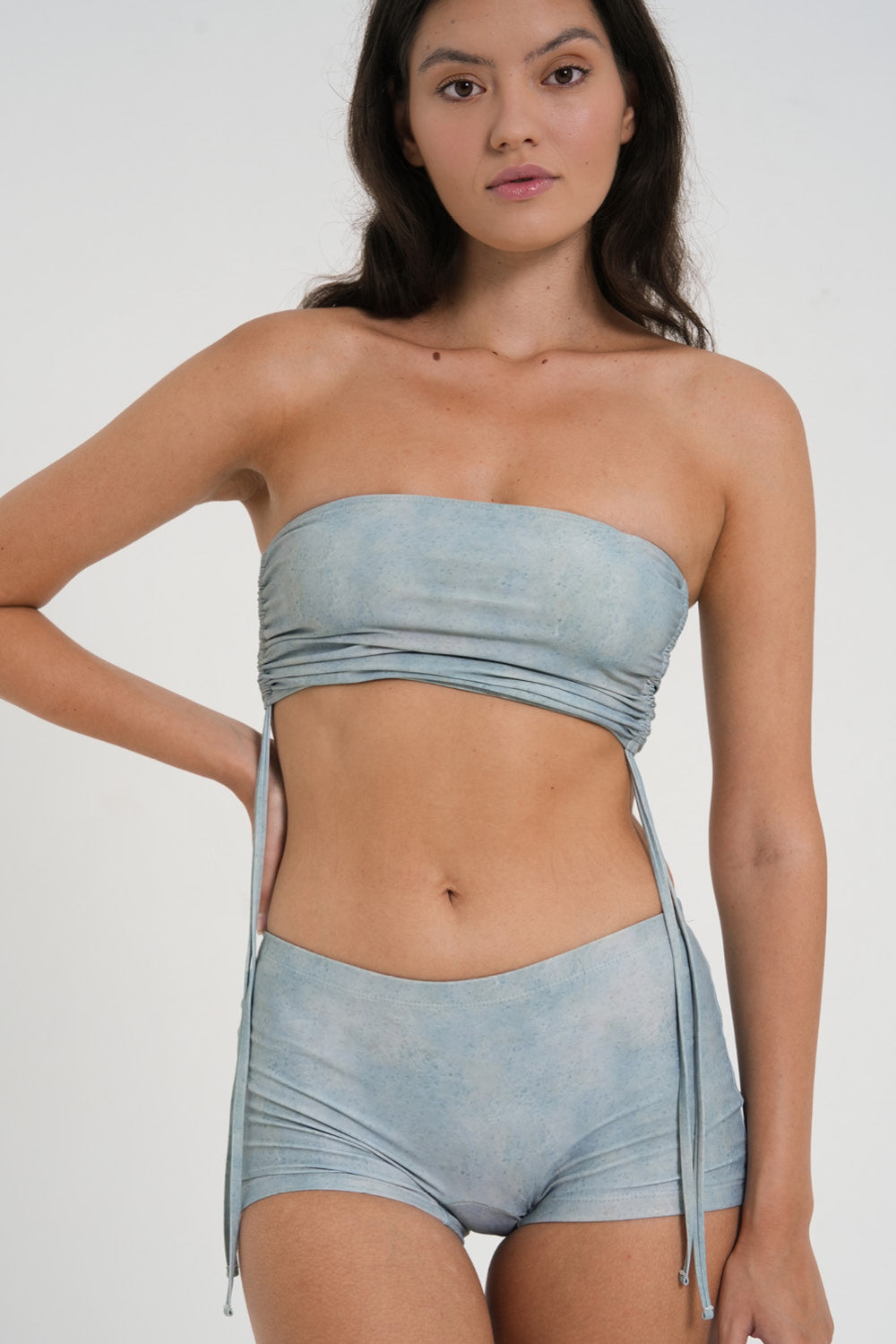 woman wearing minimalist blue green tankini top with rouched side seams and matching low rise swim shorts, sustainable swimwear to swim and surf in.