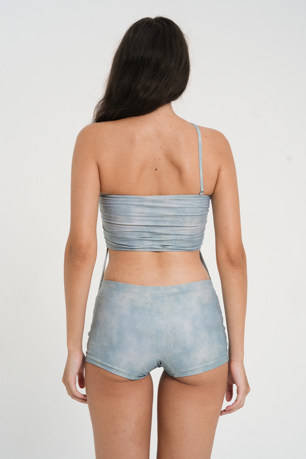 woman wearing minimalist blue green tankini top with rouched side seams and matching low rise swim shorts, sustainable swimwear to swim and surf in.