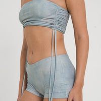 woman wearing minimalist blue green tankini top with rouched side seams and matching low rise swim shorts, sustainable swimwear to swim and surf in.