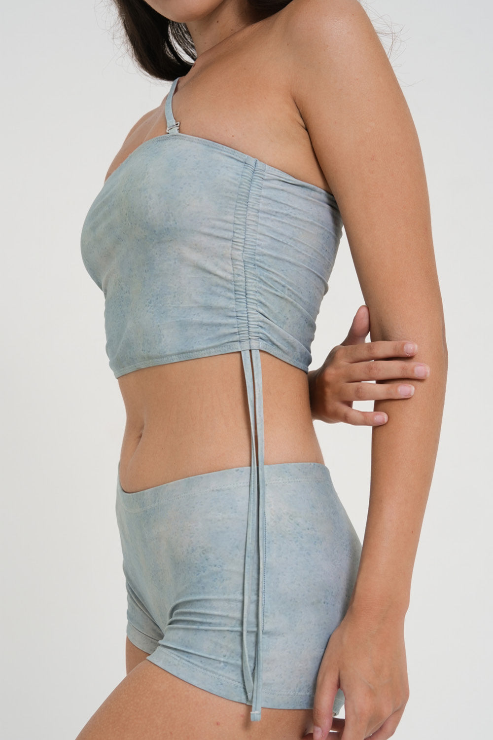 woman wearing minimalist blue green tankini top with rouched side seams and matching low rise swim shorts, sustainable swimwear to swim and surf in.