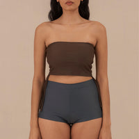 Woman wearing blueish grey high waist surf shorts, sustainable swimwear designed to stay on in the surf, offering supportive coverage and a flattering fit for active beach days.