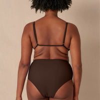 A high-waisted brown sustainable swimwear bikini bottom with minimalist design and moderate coverage, modelled by a woman in a matching bikini top.