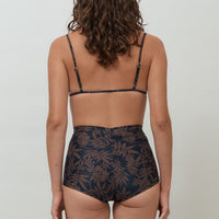 A woman wearing a black and brown leaf print triangle bikini top with adjustable straps and removable cups.
