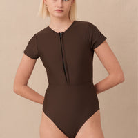 Woman wearing brown Chacahua Surf Suit — a sustainable one piece swimsuit with a flattering cut-out back, cap sleeves for sun protection and designed to stay put in the surf. Minimalist swimwear meets high-performance style.