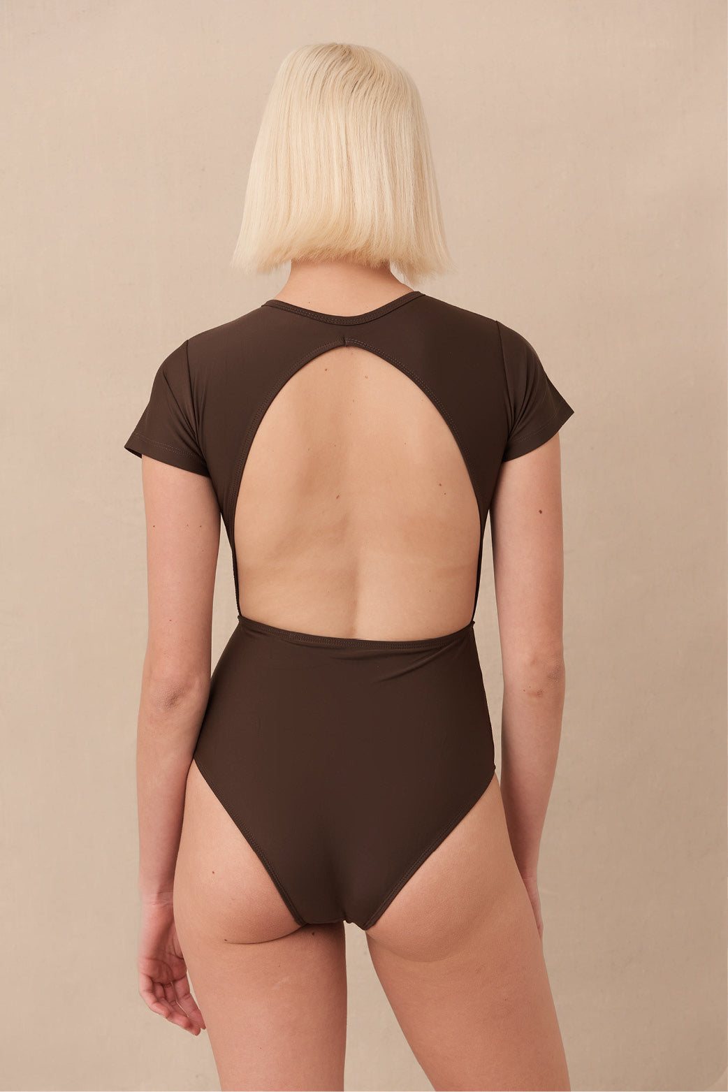 Woman wearing brown Chacahua Surf Suit — a sustainable one piece with a flattering cut-out back, designed to stay put in the surf. Minimalist swimwear meets high-performance style.