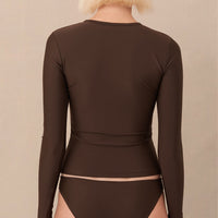 A woman wearing a brown sustainable swimwear classic brief style bikini bottom with a long sleeve rashguard.