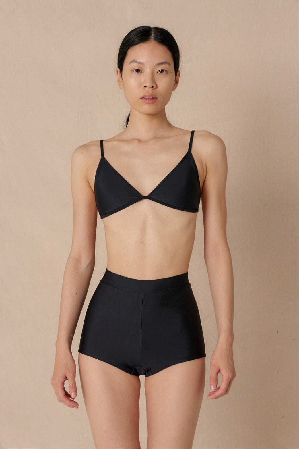 Woman wearing a black triangle bikini top with adjustable straps and removable cups, paired with matching bottoms made with sustainable swimwear fabrics.