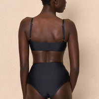 A high-waist black sustainable swimwear bikini bottom with minimalist design and moderate coverage, modelled by a woman in a matching bikini top.