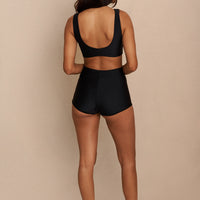 Woman wearing black high waist surf shorts, sustainable swimwear designed to stay on in the surf, offering supportive coverage and a flattering fit for active beach days.