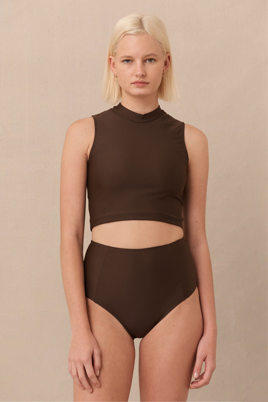 A high-waisted brown sustainable swimwear bikini bottom with minimalist design and moderate coverage, modelled by a woman in a matching bikini top.