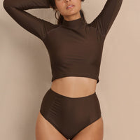 A high-waisted brown sustainable swimwear bikini bottom with minimalist design and moderate coverage, modelled by a woman in a matching bikini top.