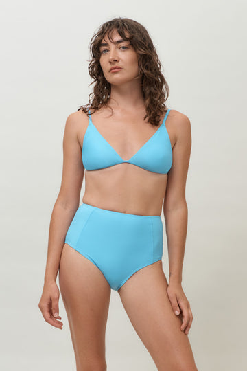 A woman wearing a lake blue triangle bikini top, a sustainable swimwear top featuring adjustable straps and removable cups, along with a matching high-waisted bottom.