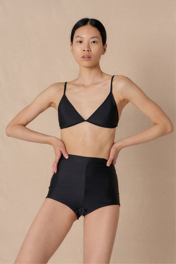 Woman wearing black high waist surf shorts, sustainable swimwear designed to stay on in the surf, offering supportive coverage and a flattering fit for active beach days.