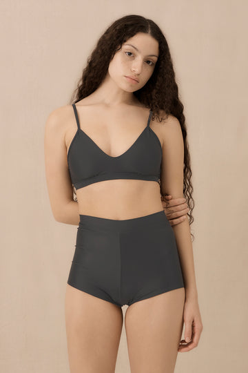 Woman wearing blueish grey high waist surf shorts, sustainable swimwear designed to stay on in the surf, offering supportive coverage and a flattering fit for active beach days.