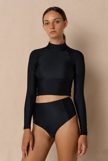 Woman wearing black Aire Turtle Neck a high neck, minimalist long sleeve women’s rashguard made from sustainable fabric, designed for sun protection and surf performance.